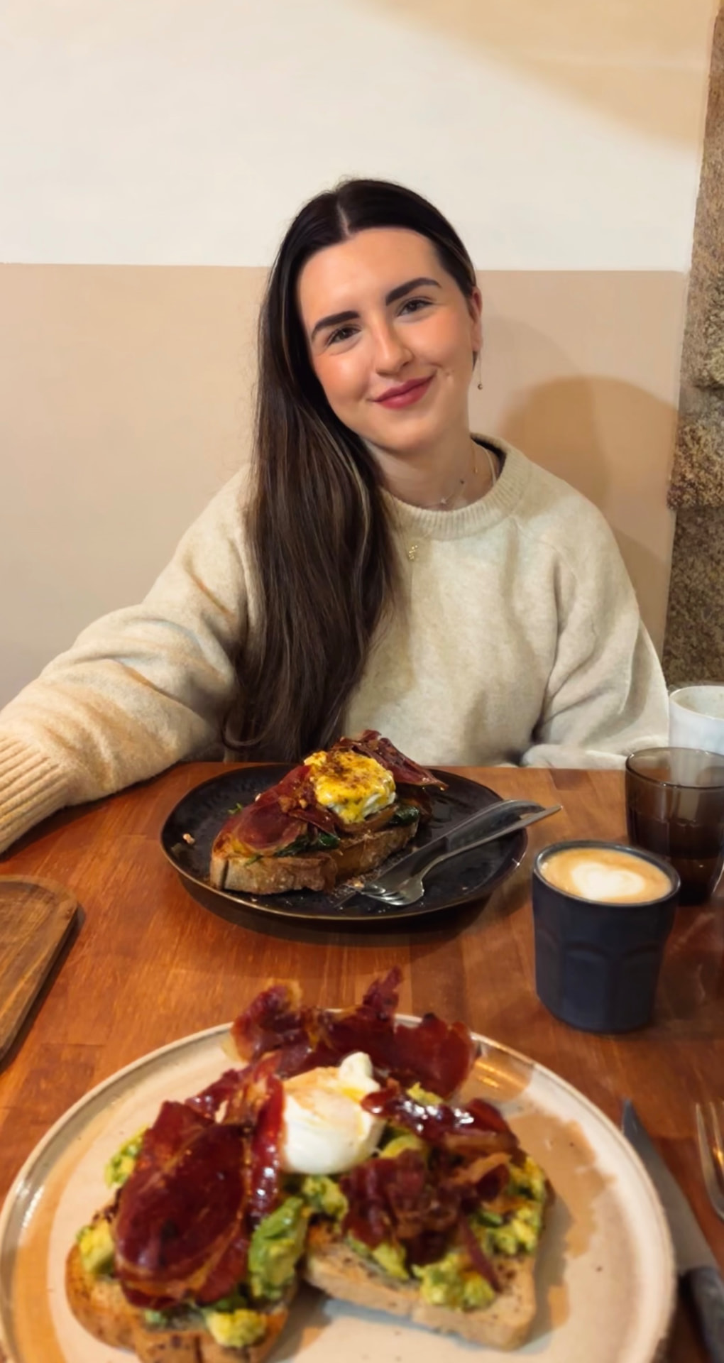 Laura García sentada en una cafetería con luz cálida, jersey crema y taza de café